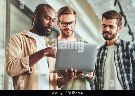 Three multiracial male colleagues looking at laptop screen Stock Photo