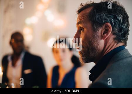 Close-up of mature man talking in dinner party with friends in background Stock Photo
