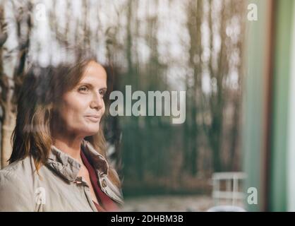 Smiling mature female professional thinking while looking through window at office Stock Photo