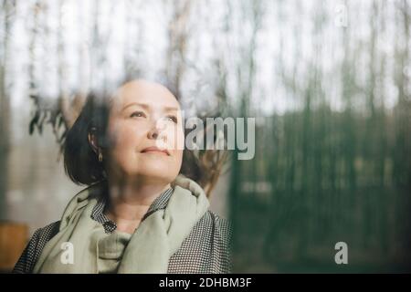 Thoughtful businesswoman looking through window at workplace Stock Photo