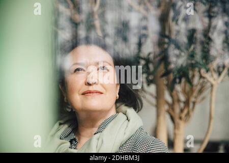 Mature businesswoman thinking while looking through window at workplace Stock Photo