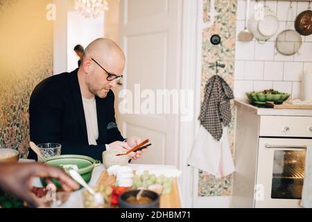 Mature man using mobile phone while sitting at dining table during party Stock Photo