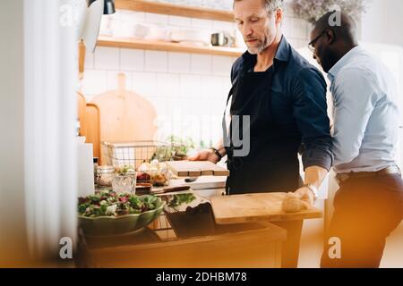 Mature man working at counter while standing with friend in kitchen Stock Photo