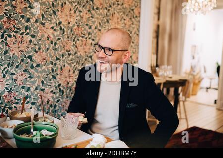 Smiling mature man looking away while sitting with food at table Stock Photo