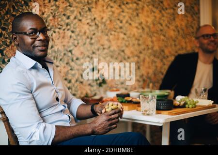 Portrait of man having food while sitting with friend by wall at home Stock Photo
