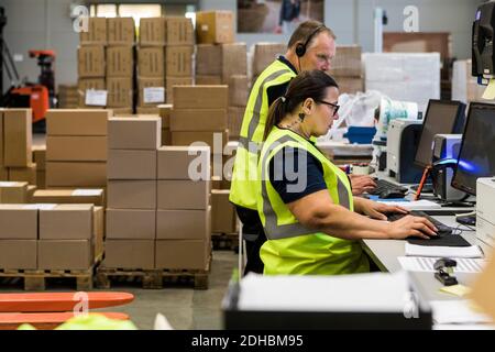 Side view of confident workers using computers at desk in distribution warehouse Stock Photo