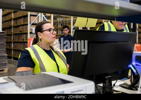 Confident mature female worker standing by coworker in distribution warehouse Stock Photo