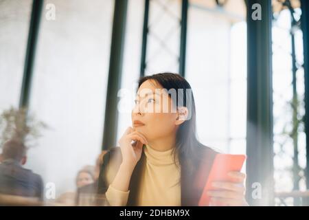Thoughtful businesswoman holding smart phone while looking away at cafeteria in office Stock Photo