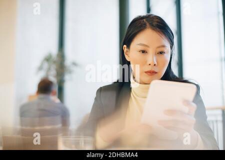 Confident mid adult businesswoman using digital tablet sitting at cafeteria in office Stock Photo