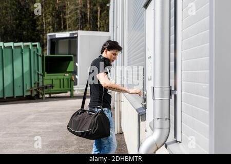 Side view of young man with duffel bag standing outside warehouse Stock Photo