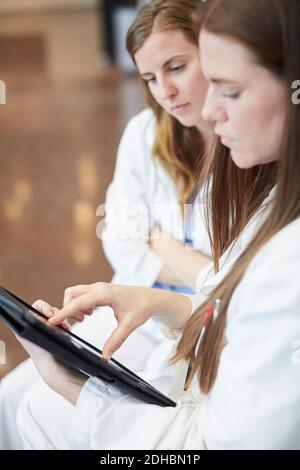Confident female doctors discussing over digital tablet in corridor at hospital Stock Photo