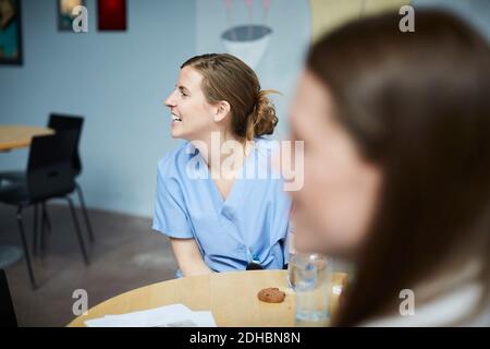 Smiling female medical workers looking away while sitting at table in hospital cafeteria Stock Photo