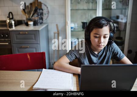 Boy wearing headphones while using laptop during homework at home Stock Photo
