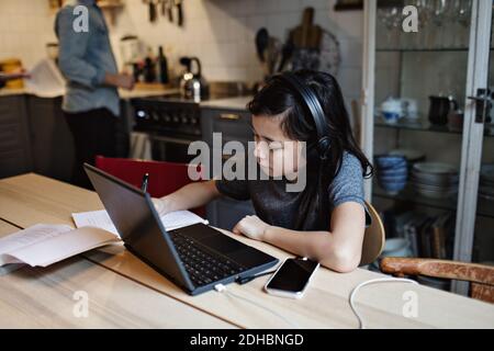 Serious boy doing homework while using laptop and mobile phone at home Stock Photo