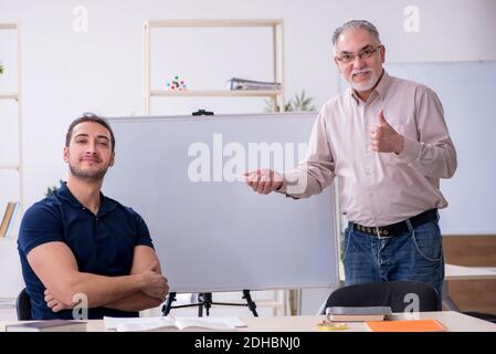 Old teacher and young male student in the classroom Stock Photo