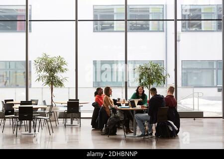 Full length of students talking while sitting at table in university Stock Photo