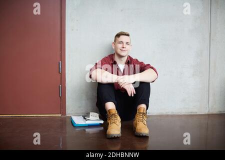 Full length portrait of male student sitting on floor against wall in university Stock Photo