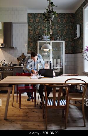 Father assisting son in studying on table at home Stock Photo
