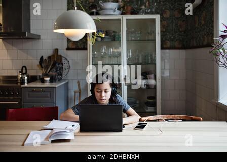 Serious boy wearing headphones while using laptop during homework at home Stock Photo