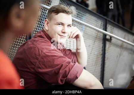 Portrait of smiling young student sitting on steps by railing at university Stock Photo