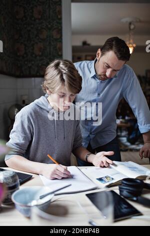 Father looking at son doing homework on table Stock Photo