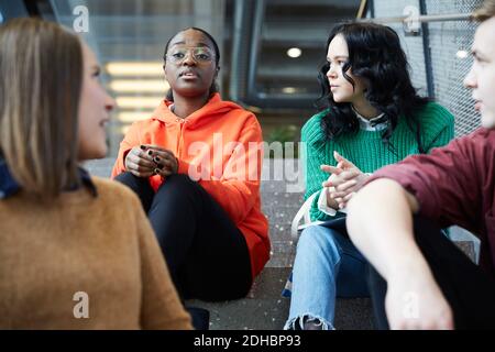 Multi-ethnic students talking while sitting on steps at university Stock Photo