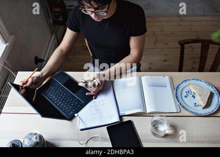 High angle view of young man having sandwich while studying on table at home Stock Photo