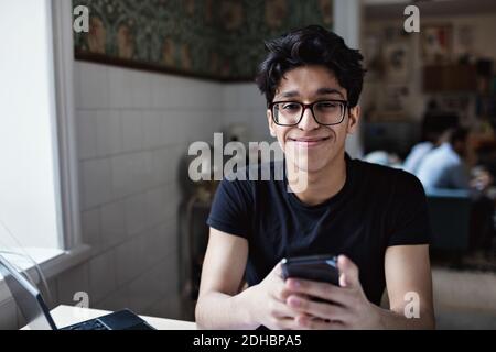 Portrait of smiling young man using social media on mobile phone while studying at home Stock Photo