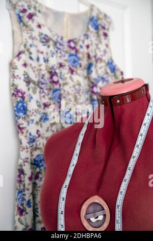 Dress form and tape measure with dress hanging behind Stock Photo