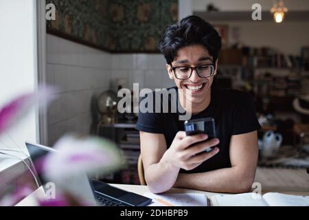 Smiling young man using social media while doing homework at home Stock Photo