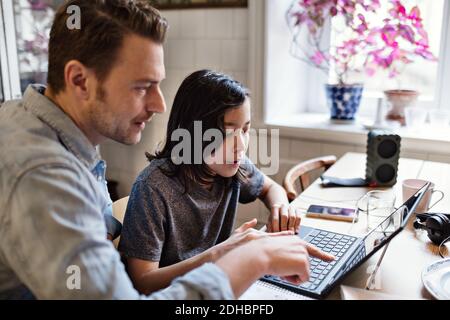 Father pointing at laptop while helping son in doing homework Stock Photo