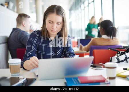 Female student using laptop at table with friends in background Stock Photo