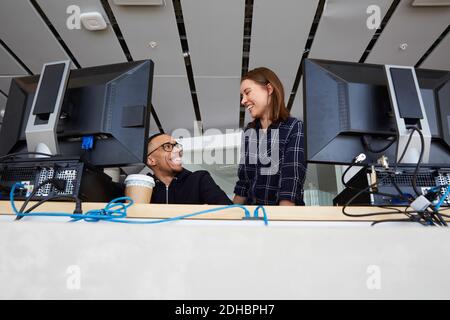 Low angle view of smiling friends talking while using computers at university Stock Photo