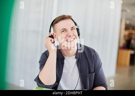 Smiling male student with headphones studying in university cafeteria Stock Photo