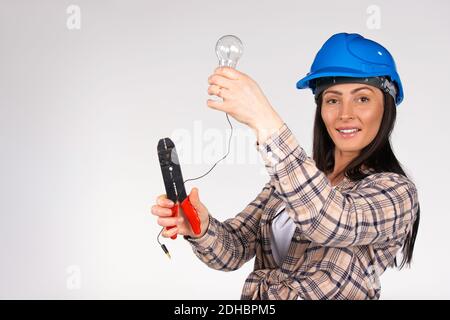 A woman electrician repairs a light with a light bulb in hands and looks with a smile at the camera. White background. Stock Photo