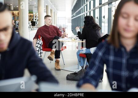 Friends talking while studying together at table in university cafeteria Stock Photo