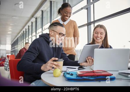 Happy young friends looking at digital tablet while studying at table in university Stock Photo