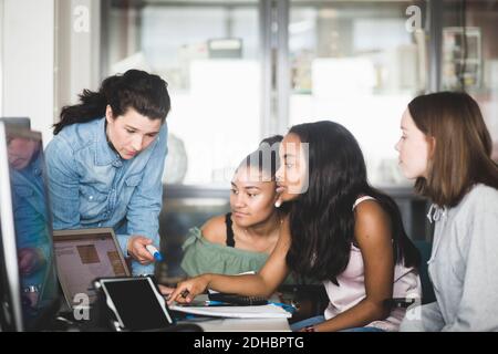 Mature teacher and female students discussing over laptop in computer lab at high school Stock Photo