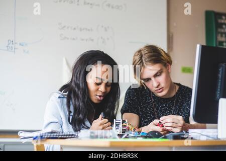 Confident female student preparing science project with young male friend on desk in classroom at high school Stock Photo