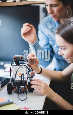 Female teacher assisting teenage student preparing robot on desk in classroom at high school Stock Photo
