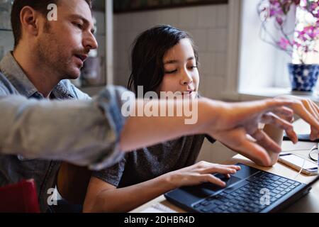 Father assisting son in using laptop for homework at home Stock Photo