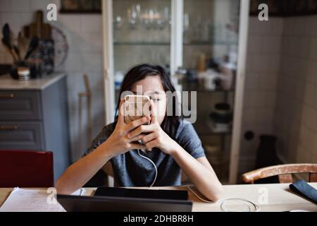 Boy using smart phone while doing homework at home Stock Photo