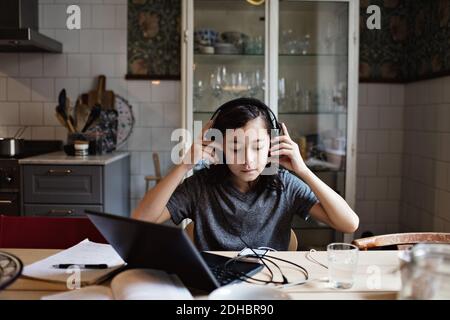 Boy using headphones while doing homework at home Stock Photo