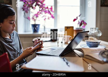 Serious boy using mobile phone while studying at home Stock Photo