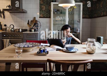 Boy drinking water while using laptop for homework at home Stock Photo