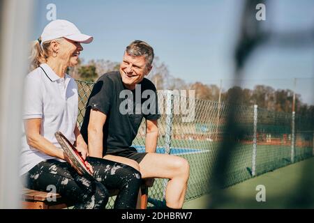 Happy senior man and woman talking while sitting on bench at tennis court Stock Photo