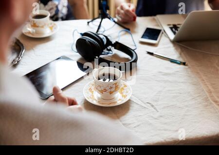 Cropped image of senior man having coffee while vlogging with friends at table Stock Photo