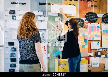 Female colleagues discussing over strategy on wall at creative office Stock Photo