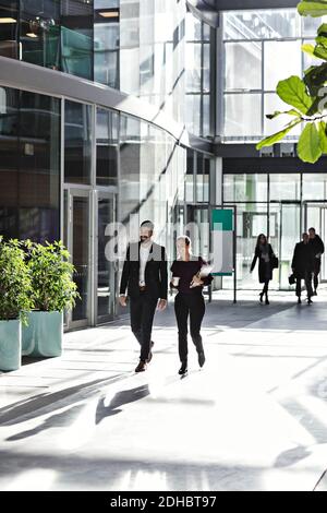 Full length of smiling business coworkers talking while walking in atrium Stock Photo