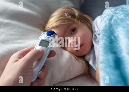 Parent takes temperature for her child with infrared thermometer at home, low-grade fever Stock Photo